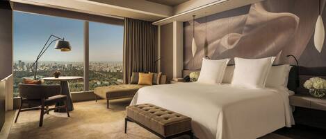 A modern hotel room with a large bed, a sitting area with a view, and a cityscape visible through the window.