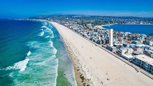 Un paisaje urbano costero con una playa extensa, edificios residenciales densos y un cielo azul despejado.