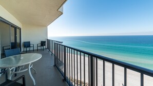 A balcony with a glass table and chairs, overlooking a beach and ocean. - Rest Ashored Commodore 1303-Beachfront Master-Rest Assured, You'll Love It Here! (Panama City Beach)