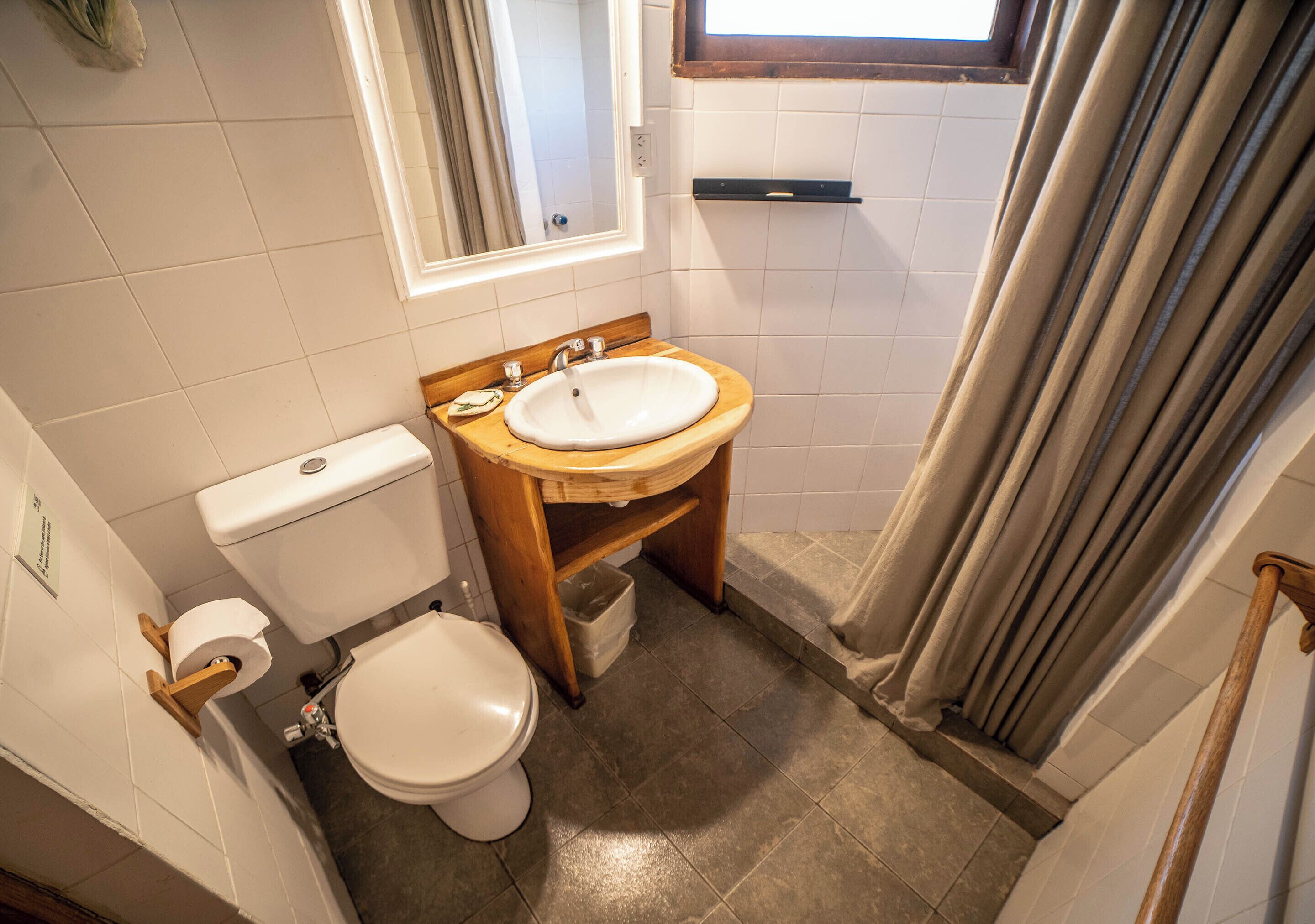 Un baño pequeño con inodoro blanco, lavamanos de madera y zona de ducha.