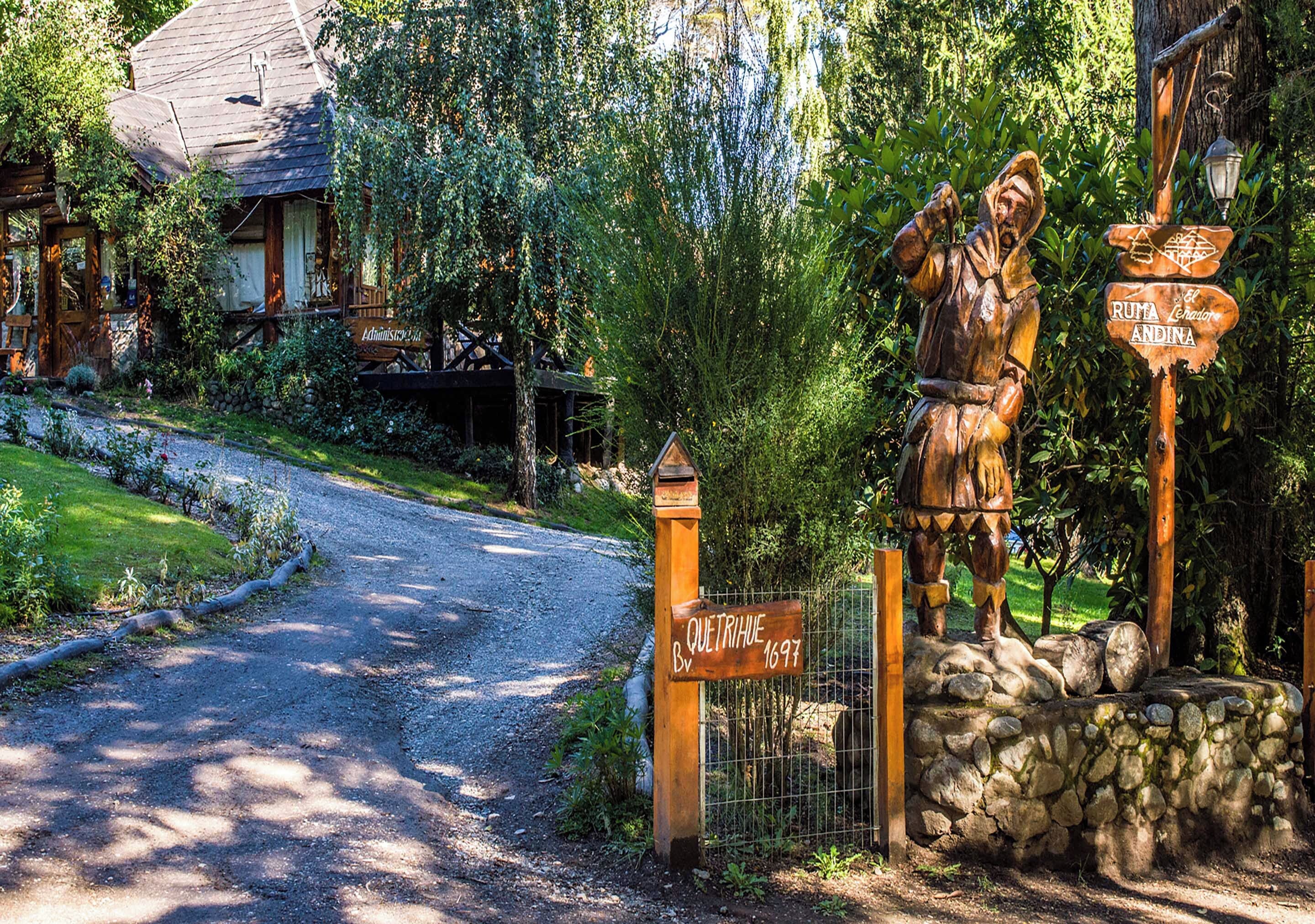 A rustic wooden signpost with directional signs, a stone wall, and a wooden fence at a rural entrance.