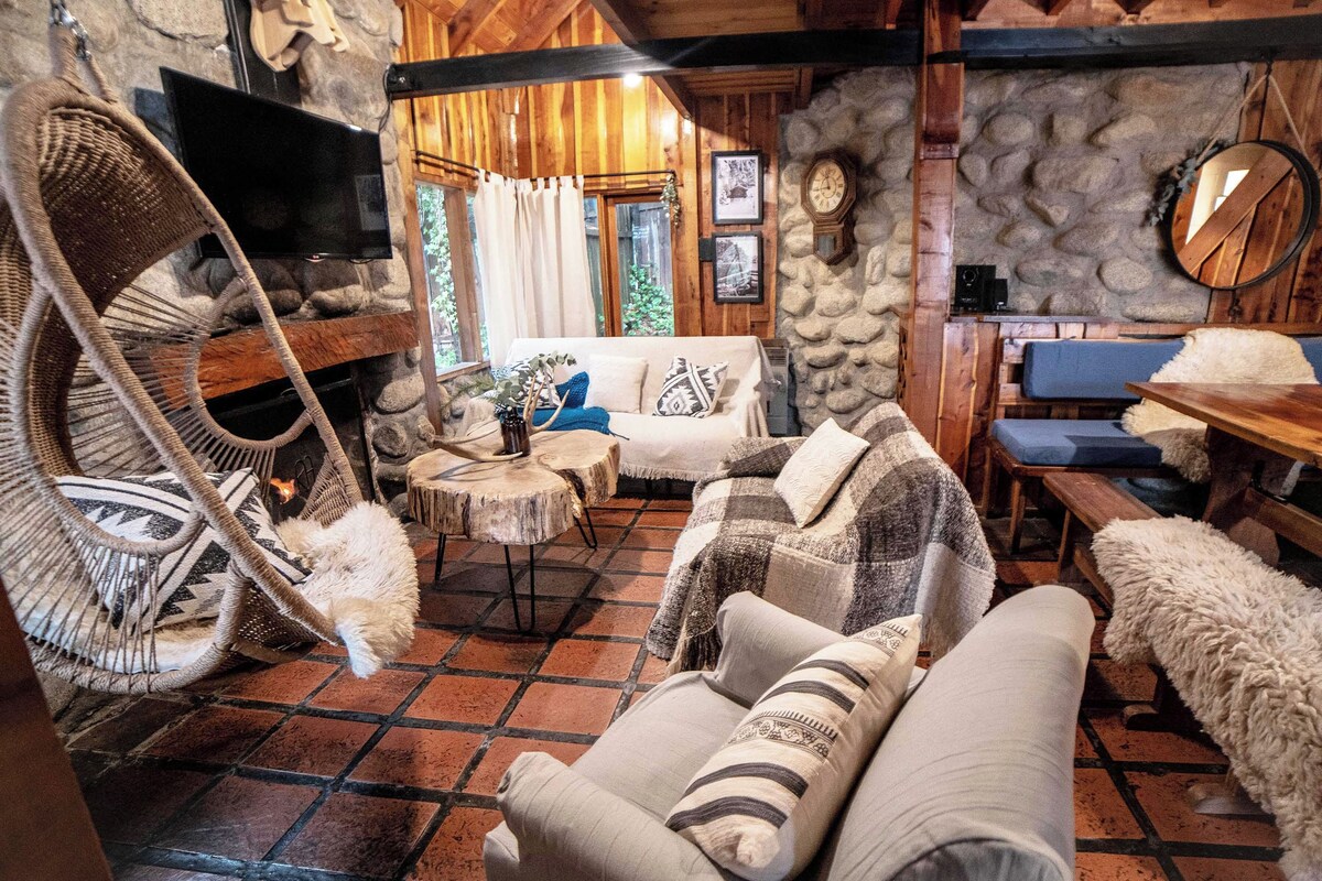 L’intérieur chaleureux d’un chalet avec un mur en pierre, des meubles en bois, un téléviseur et une cheminée en pierre.