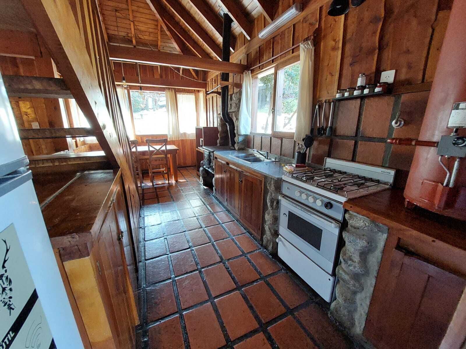A rustic kitchen with wooden beams, a gas stove, a sink, and a refrigerator.
