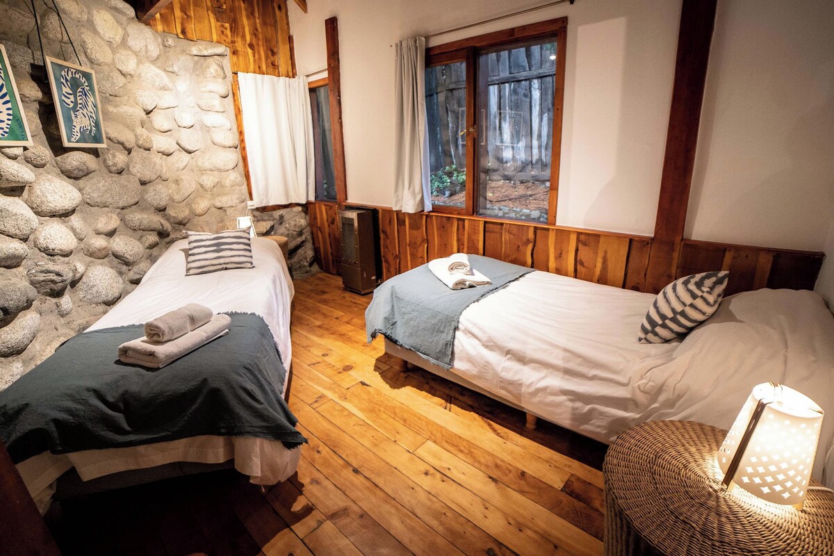 Une chambre rustique avec deux lits, des murs en bois, un mur en pierre et une fenêtre avec des rideaux.