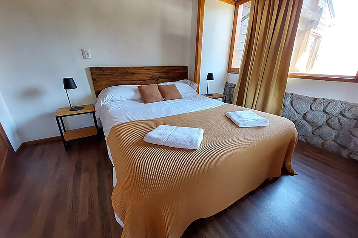 Un lit bien fait, avec une tête de lit en bois, deux tables de chevet avec des lampes et un mur en pierre.