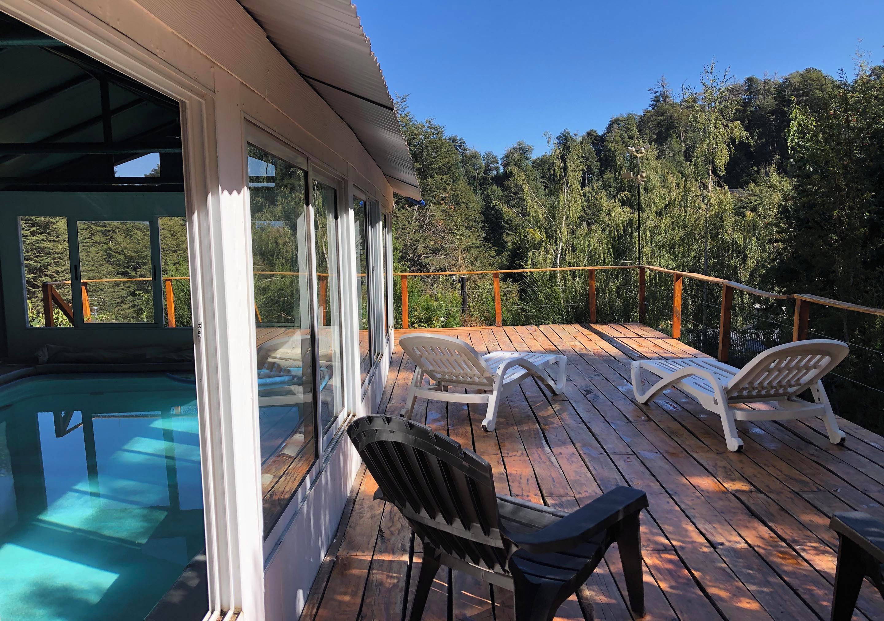 Una terraza de madera con sillones de descanso y una piscina.