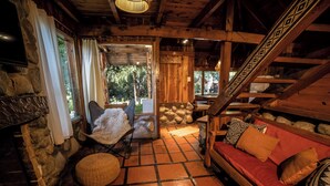 A cozy cabin interior with a stone fireplace, wooden walls, a red sofa, and a stone bench. - Ruma Andina by DOT Cabana (Villa La Angostura)