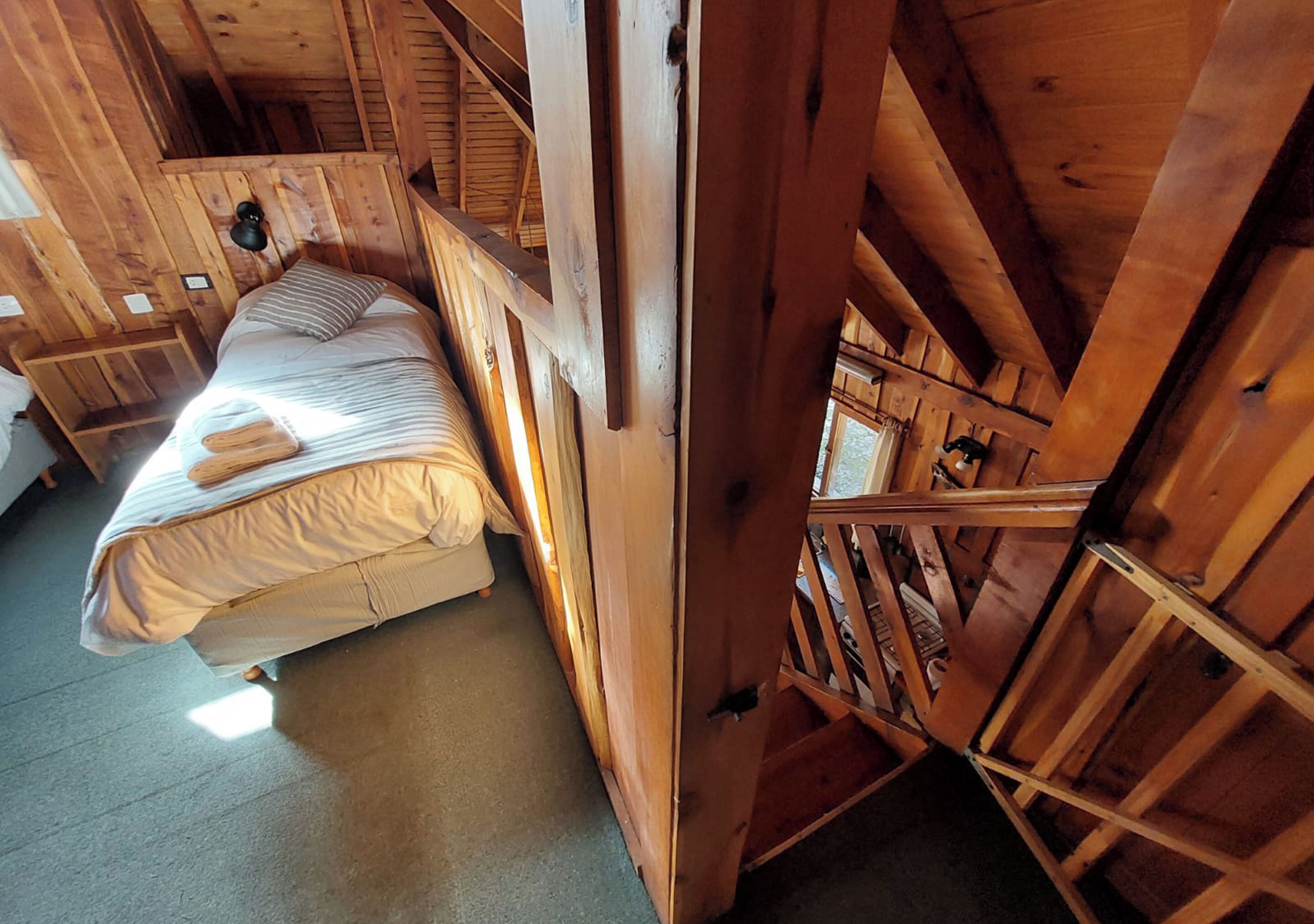 A wooden cabin room with a bed, a window, and a wooden ladder.