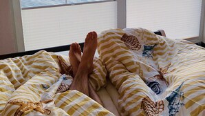 A bed with striped bedding and a view of the sea through a balcony. - Houseboat "ELANDI" - relaxation, fun & luxury (Bitterfeld)