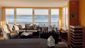 A living room with a large window overlooking a body of water, striped sofas, a small table, and a decorative lantern. - Houseboat "ELANDI" - relaxation, fun & luxury (Bitterfeld)