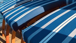 A sunlit deck with striped lounge chairs and a table, overlooking a calm body of water. - Houseboat "ELANDI" - relaxation, fun & luxury (Bitterfeld)