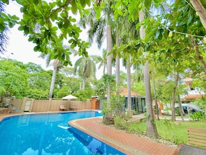 A swimming pool surrounded by lush greenery and palm trees, with a brick pathway leading to a covered seating area. - E-Outfitting Golden Country Hotel (Mandalay)