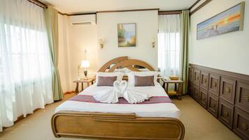 A hotel room with a large bed, two bedside tables, a wall-mounted air conditioner, and a painting above the bed.