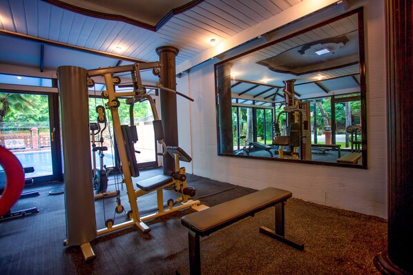 A gym with exercise equipment, a bench, and a large mirror reflecting the gym area.