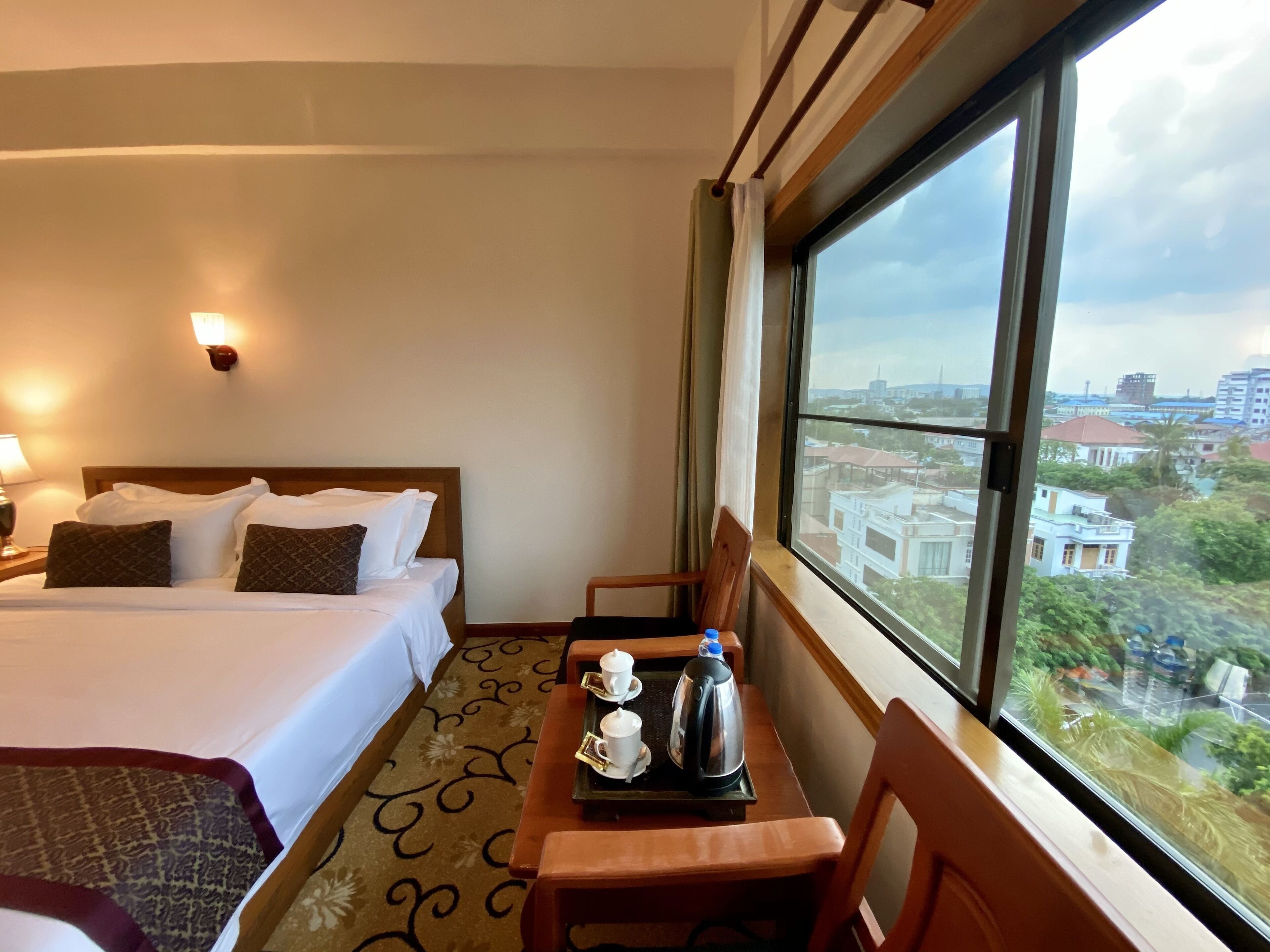 A hotel room with a bed, a table with a tray of breakfast items, and a large window offering a city view.