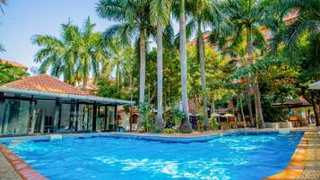 Relax by the serene pool surrounded by lush palm trees and shaded seating areas.