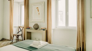 A hotel room with a bed, a chair, a desk with a vase and books, and a window with curtains. - Bright and Spacious Apt on the City Centre (Lisboa)