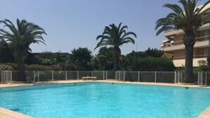 Ein rechteckiger Swimmingpool mit klarem, blauem Wasser, umgeben von einer gefliesten Liegefläche und einem Metallzaun.