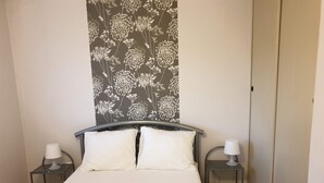 Ein Schlafzimmer mit einem Bett, zwei Nachttischen, einer Lampe auf jedem Tisch und einem Wandbehang mit floralem Muster über dem Bett.
