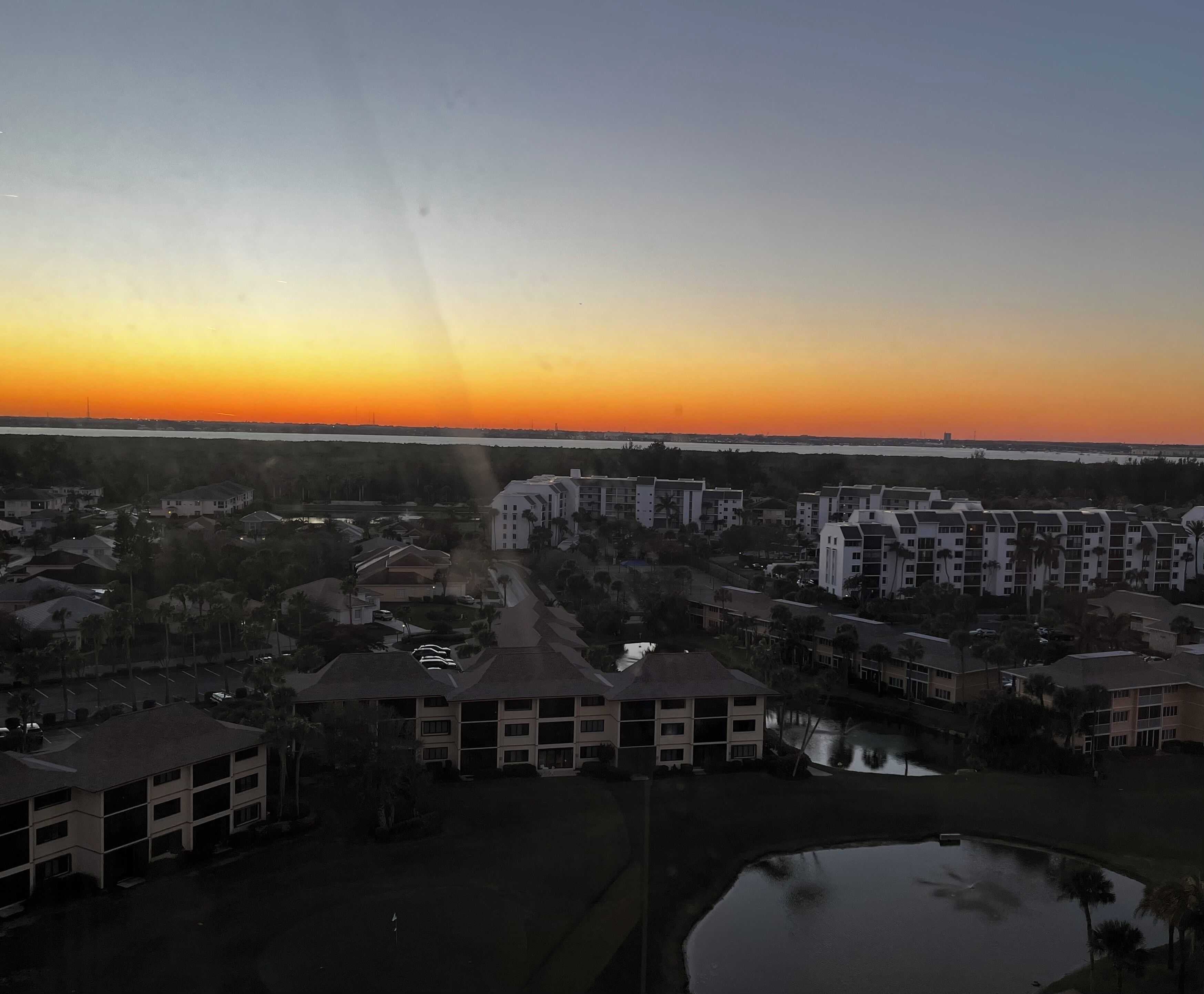 A residential area with multiple apartment buildings, a small body of water, and a clear sky.