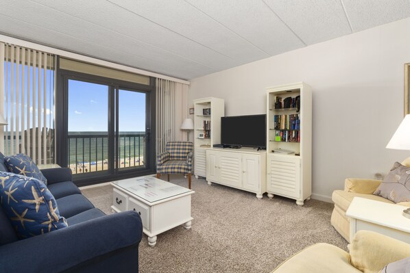 A hotel room with a balcony, a sofa, a coffee table, a TV, and a bookshelf.