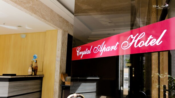 A hotel reception area with a reception desk, a glass partition, and a sign reading "Crystal Apart Hotel". - Crystal Apart Hotel (Macaé)