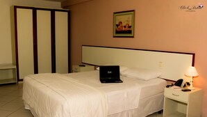 A hotel room with a bed, a nightstand, a laptop, a lamp, and a wardrobe. - Crystal Apart Hotel (Macaé)