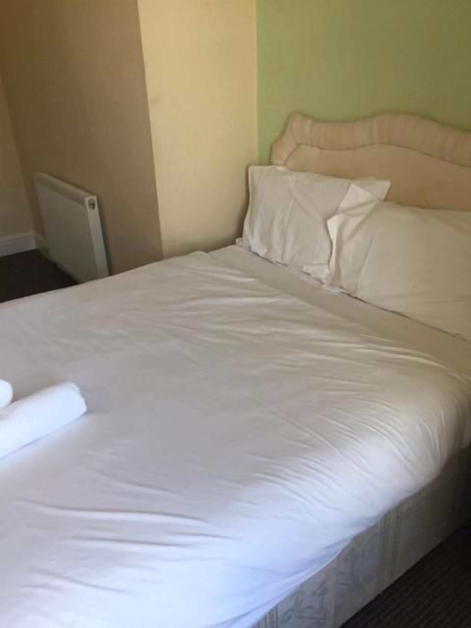 A bed with a headboard, a rolled-up white blanket, and a radiator on the wall.