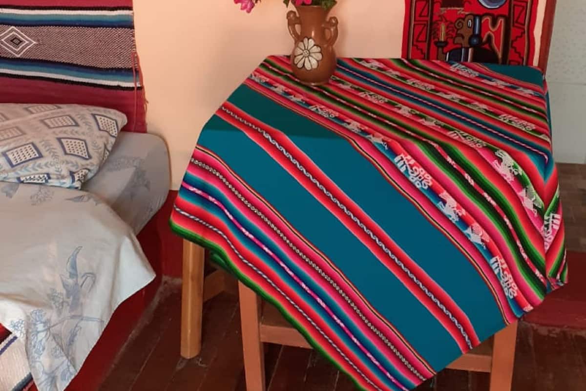 A room with a bed, a small table with a vase of flowers, and a colorful blanket.