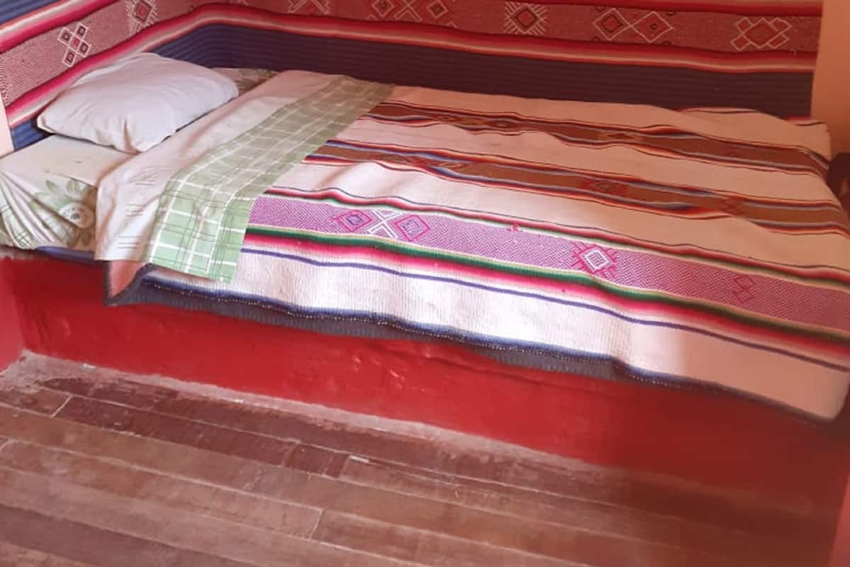 A bed with a patterned bedspread and pillows, a window with a curtain, and a wall with a decorative piece.