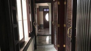 A corridor with wooden doors and windows, leading to a room with a tiled floor and a view of the sky. - Skina Comfort - Stays & Events - Large House with Pool! (Guarujá)