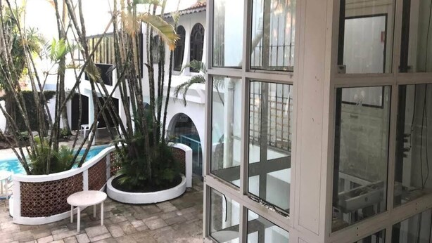 A covered outdoor area with a pool, potted plants, and a view of a building with arches. - Skina Comfort - Stays & Events - Large House with Pool! (Guarujá)