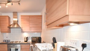 A modern kitchen with wooden cabinets, a stainless steel range hood, a built-in oven, a microwave, a toaster, and a coffee maker. - MK Hub Apartment with Oak Furniture (Milton Keynes)