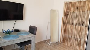 Una habitación con una televisión de pantalla plana montada en la pared, un espejo de pie, una mesa de comedor con individuales azules y una cortina decorativa.