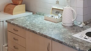 Una cocina con armarios de madera clara, encimera de granito y hervidor blanco.