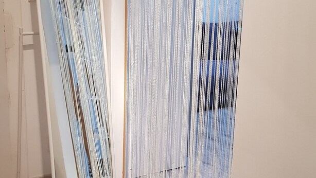 Una habitación con piso de madera, un espejo de pie, un cuadro enmarcado en la pared y una cortina con diseño vertical.