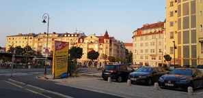 A parking area with several cars, a yellow sign with text, and buildings in the background. - Ksenia Apartment (Karlovy Vary)