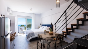 A modern bedroom with a bed, a dining table with chairs, and a staircase. - Evilio Suites, Inspired Family Retreat with Pool (Prinos, Rethymno)