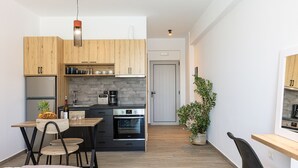 A compact kitchen with wooden cabinets, a built-in oven, and a dining area with a table and chairs. - Evilio Suites, Inspired Family Retreat with Pool (Prinos, Rethymno)