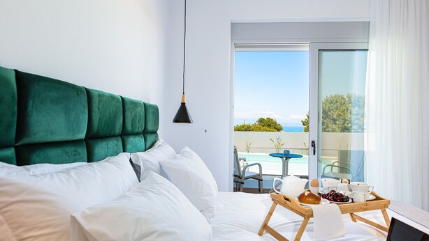 A hotel room with a bed, a laptop, a tray with breakfast items, and a view of a pool and sky. - Evilio Suites, Inspired Family Retreat with Pool (Prinos, Rethymno)