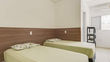 Una habitación con dos camas individuales, un cabecero de madera, una ventana con persianas, una silla y una puerta.