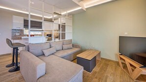 A modern living room with a sectional sofa, a coffee table, a TV on a wooden stand, and a kitchen area in the background. - 2 Bedroom Villa, Sarakina, Zakynthos (Sarakina)