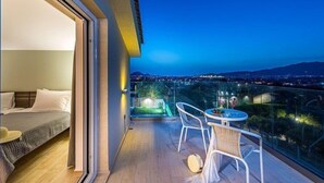 A balcony with a bed and a table with chairs, overlooking a cityscape at night. - 2 Bedroom Villa, Sarakina, Zakynthos (Sarakina)