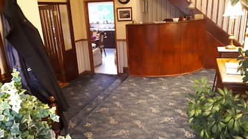 A hotel lobby with a wooden reception desk, a staircase, and a view into the dining area.