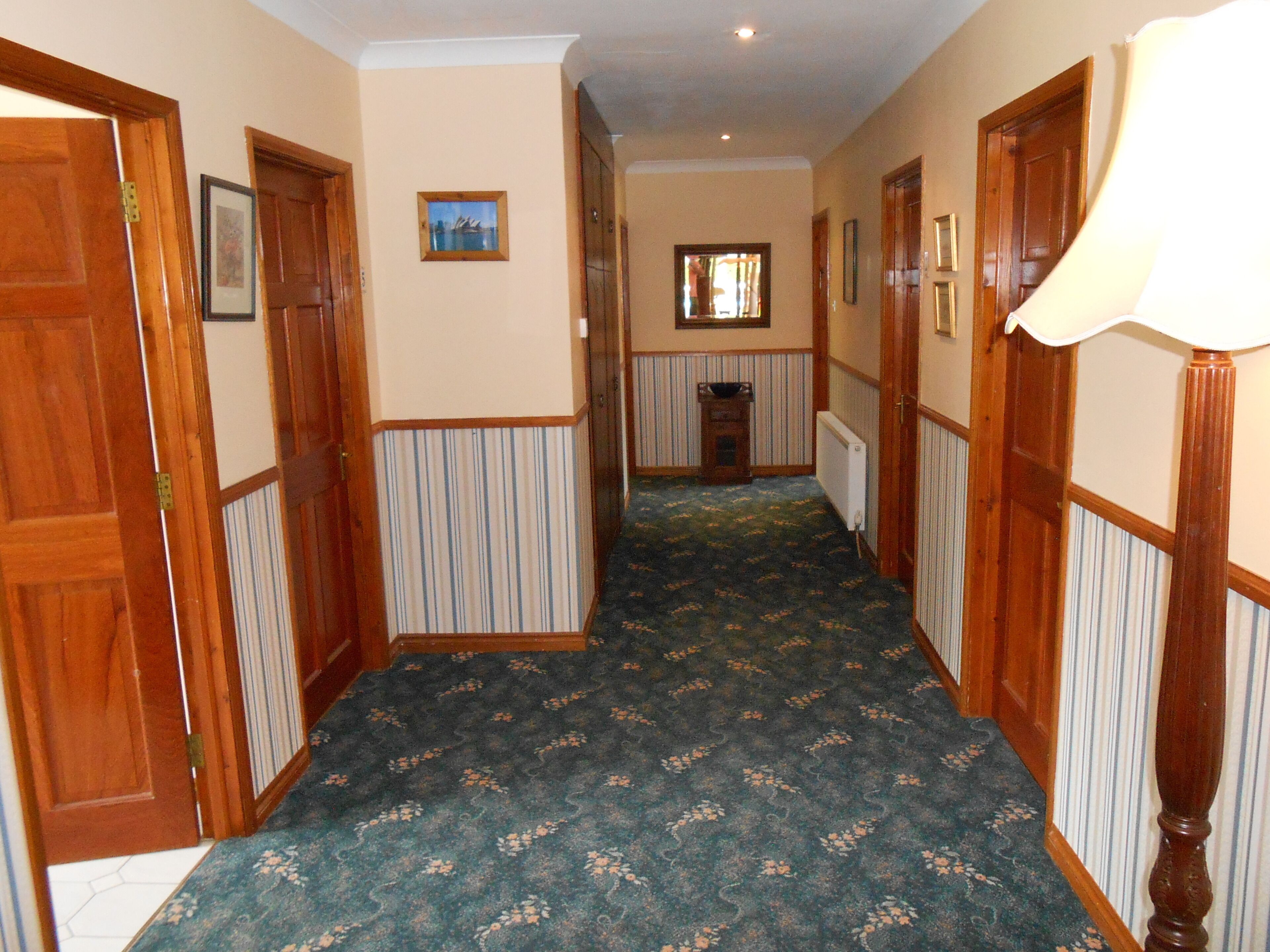 A hallway with wooden doors, striped wallpaper, and a patterned carpet.