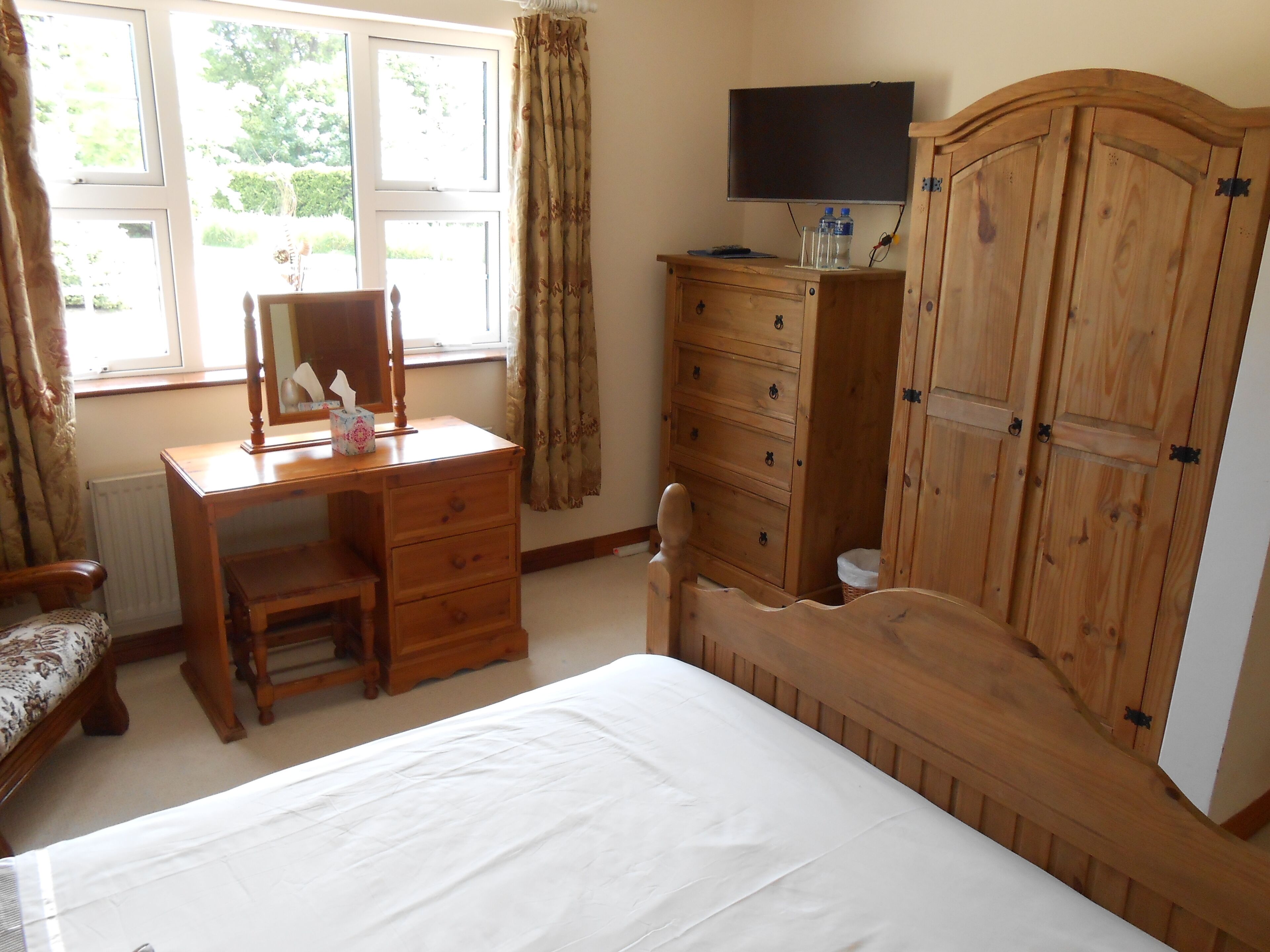A bedroom with a wooden desk, a bed, a wardrobe, and a television on a stand.