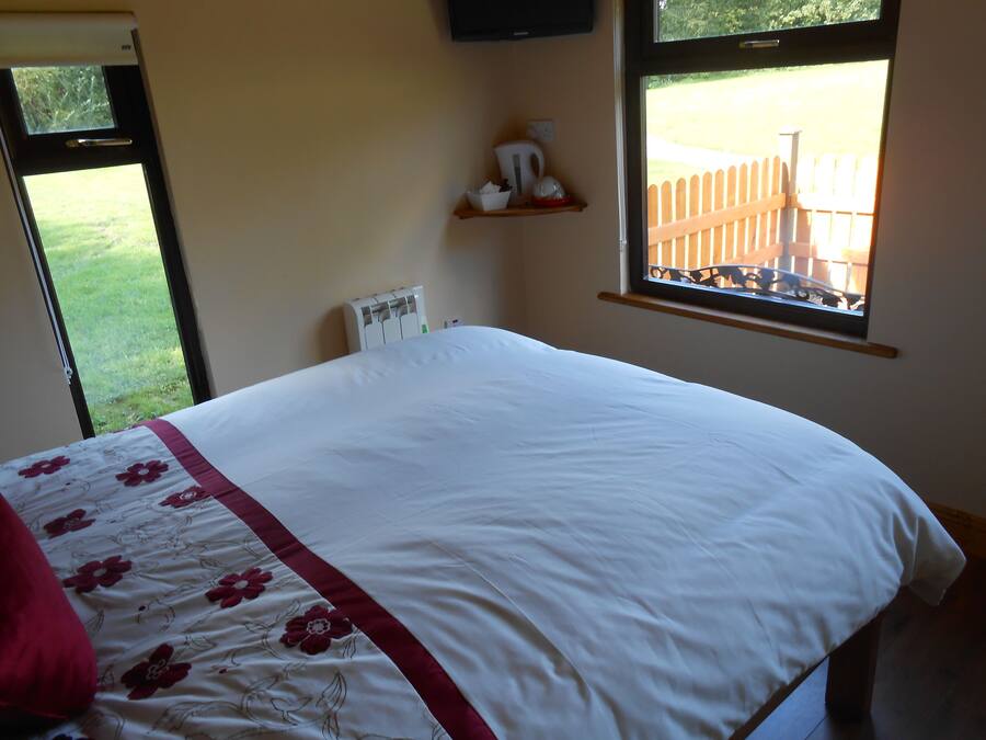 A bedroom with a bed, a window with a view of a fence, and a thermostat on the wall.