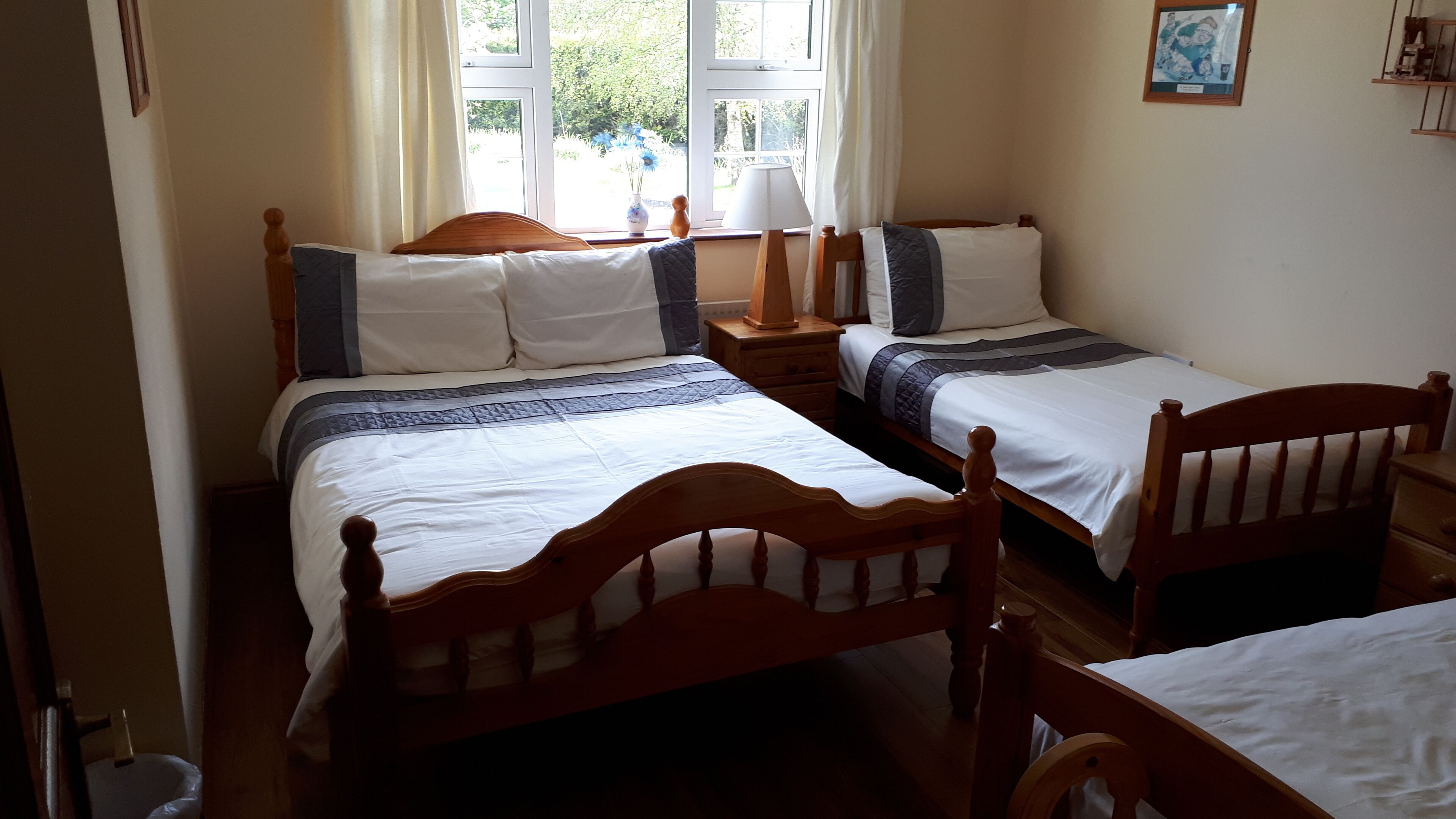 A bedroom with two wooden beds, a nightstand, a lamp, and a window with curtains.