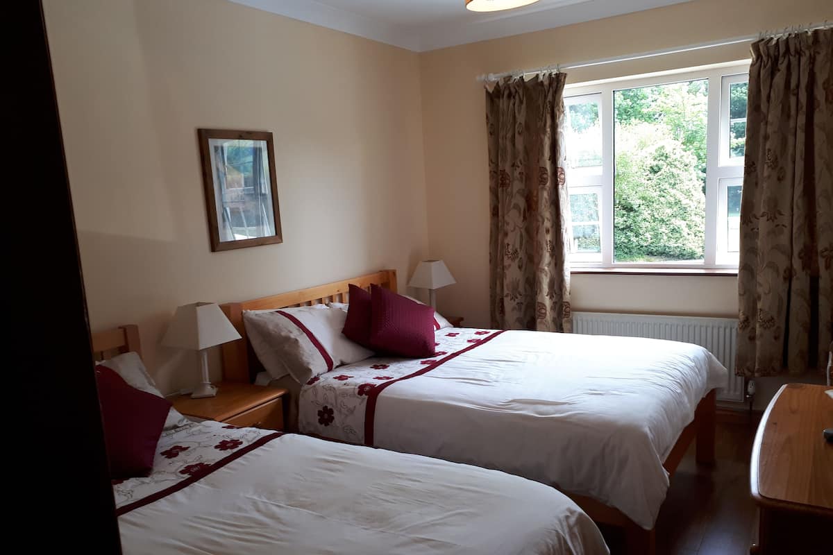 Ein Hotelzimmer mit zwei Betten, einem Fenster mit Vorhängen, einem Nachttisch mit Lampe und einem gerahmten Bild an der Wand.