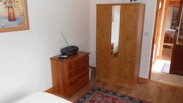 A bedroom with a wooden dresser, a TV on a stand, a bed, and a mirror in the wardrobe.
